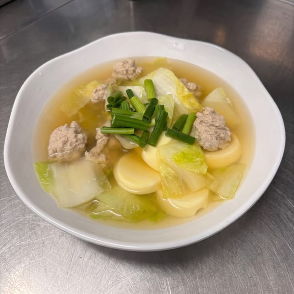 Clear soup with meatballs, cabbage, tofu, and chopped green onions in a white bowl.
