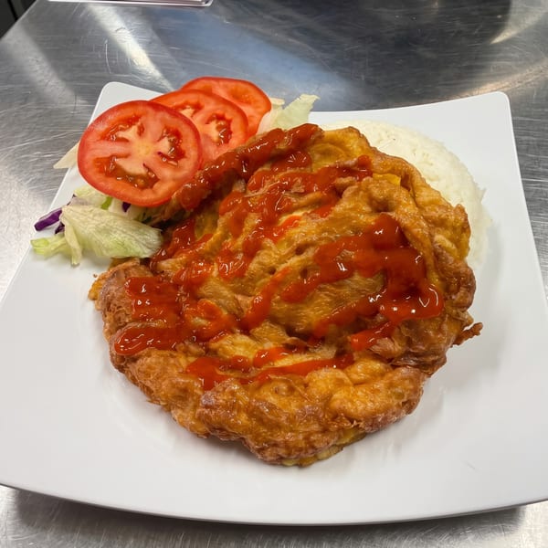 Golden-brown omelet with red sauce, white rice, sliced tomatoes, and lettuce on a white plate.