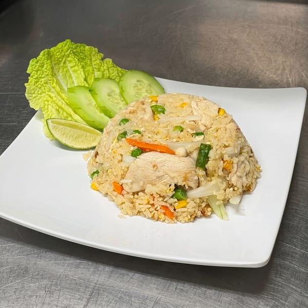 Chicken fried rice with vegetables, lettuce, cucumber, and lime on a white plate.