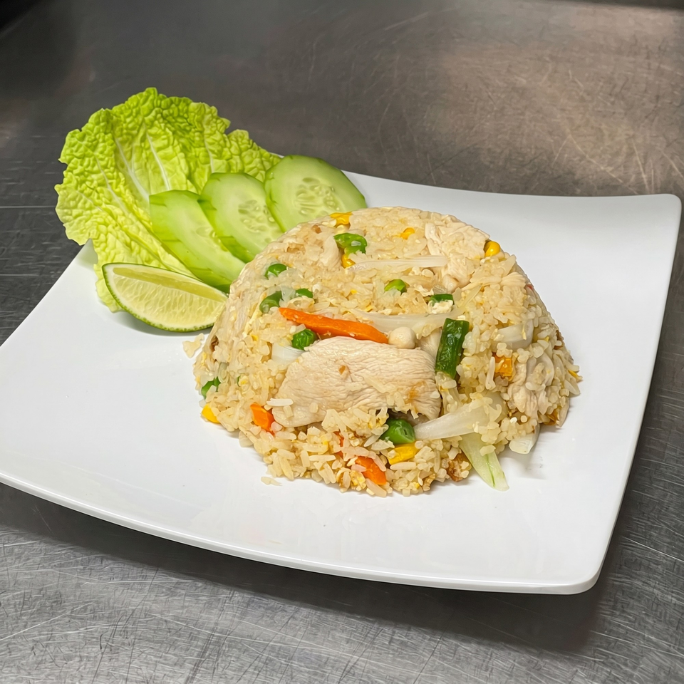 Chicken fried rice with vegetables, lettuce, cucumber, and lime on a white plate.