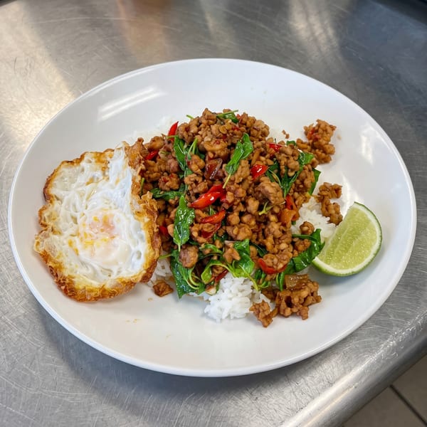 Pad Krapow with minced meat, basil, chili, fried egg, and a lime wedge on white rice.